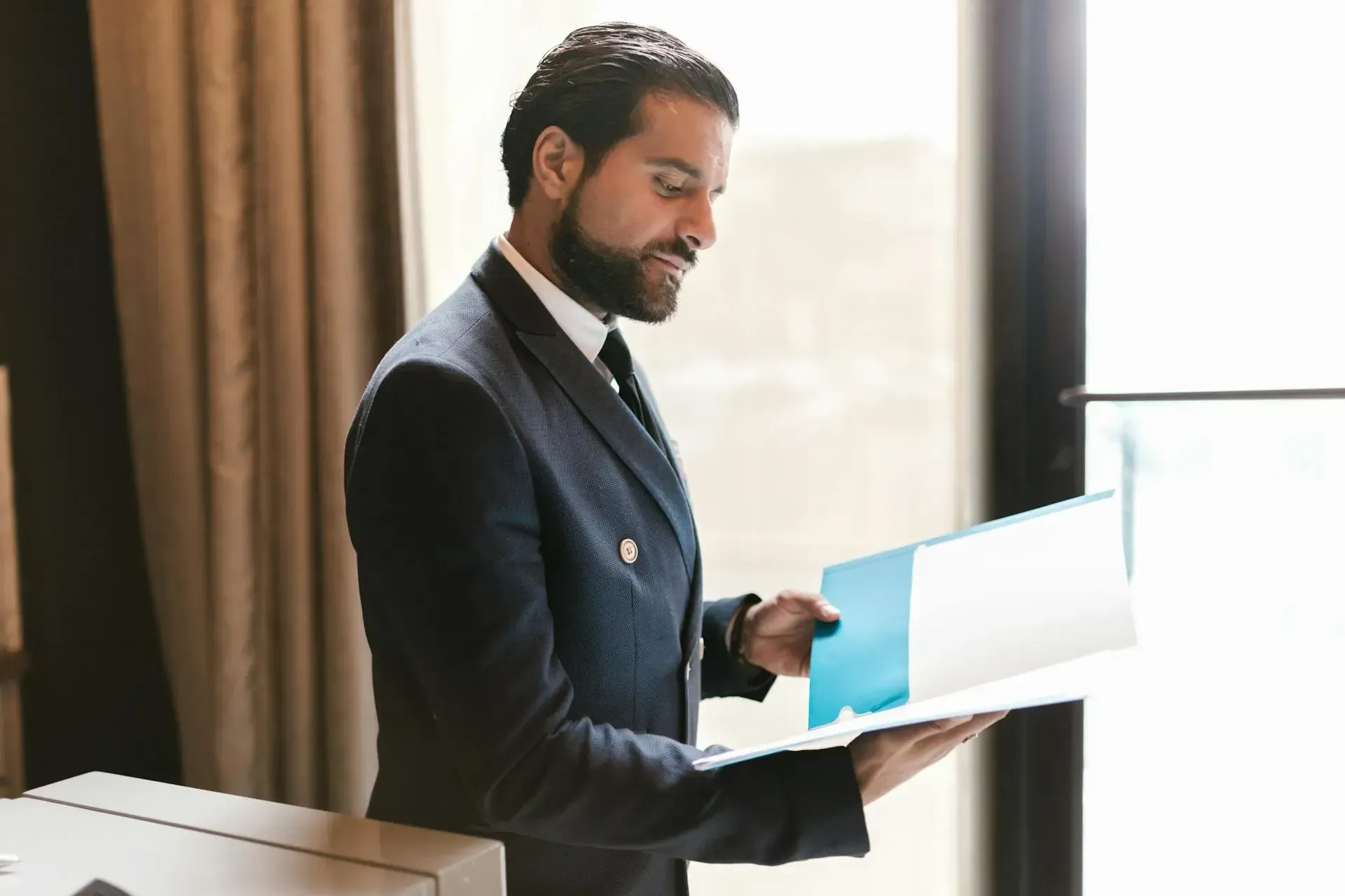 Persona con traje revisando documentos dentro de una carpeta azul en un entorno de oficina.
