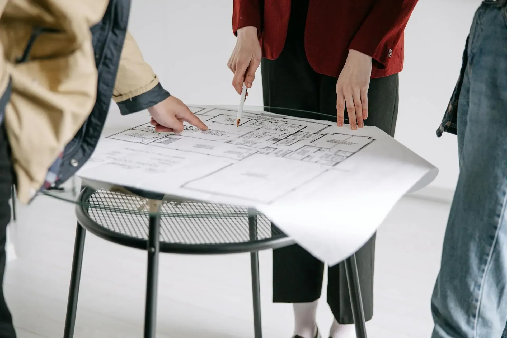 Tres personas reunidas alrededor de un plano arquitectónico, analizando y comentando diferentes áreas del proyecto.